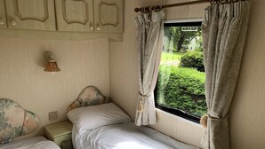 A bedroom with two beds, a window with curtains, a headboard with a floral design, and a wall-mounted light fixture.