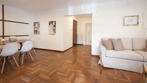 A modern living room with a wooden herringbone floor, a sofa, and a dining area with a table and chairs.