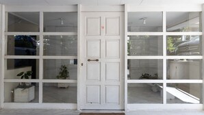 A white door with a number 18, leading to a covered entrance with glass panels and potted plants.