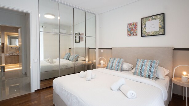 A modern hotel room with a large bed, a glass partition, a bathroom, and a bedside table with a lamp.