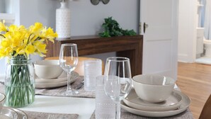 Een eettafel gedekt met transparant servies, witte borden en een vaas met gele bloemen.