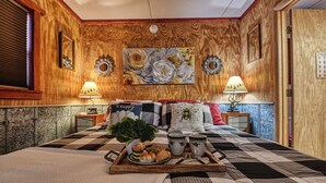 A cozy bedroom with a large bed, a wooden headboard, two bedside lamps, a tray with breakfast items, and a painting on the wall.