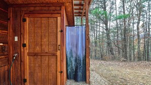 A wooden cabin with a door, a hose, and a view of a forest.