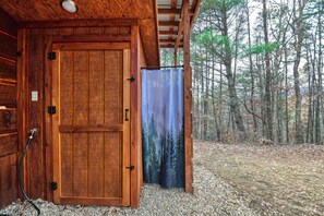 A wooden cabin with a door, a hose, and a view of a forest. - Honey Hut--OUTDOOR SHOWER--HOT TUB (Newport)