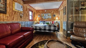 A cozy room with a wooden interior, a bed with a checkered bedspread, a red leather sofa, and a brown leather armchair.