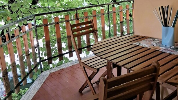 Une table et des chaises en bois sur un balcon doté d’une rambarde en métal et d’une clôture en treillis.