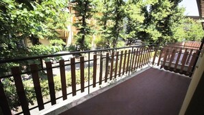 Un balcon doté d’une balustrade en bois, une vue sur la verdure et un bâtiment en arrière-plan.