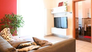 A living room with a sofa, a television, a radiator, and a plant. - CN004 - Cesenatico, new penthouse with terrace and Jacuzzi (Cesenatico)
