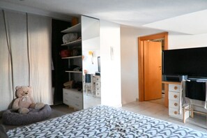Een slaapkamer met een bed, een bureau, een stoel, een kledingkast en een teddybeer.