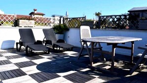 A deck with a checkered floor, a round table, and two lounge chairs. - CN004 - Cesenatico, new penthouse with terrace and Jacuzzi (Cesenatico)