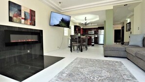 Een woonkamer met een open haard, een televisie, een bank en een eethoek met stoelen en een tafel.