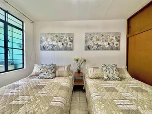 Une chambre avec deux lits, une fenêtre et deux tableaux représentant des motifs floraux accrochés au mur.