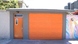 A garage with an orange door and a large garage door, adjacent to a building with a colorful mural. - La Cacho studio Free Wifi, Kitchenette, Central (Tijuana)