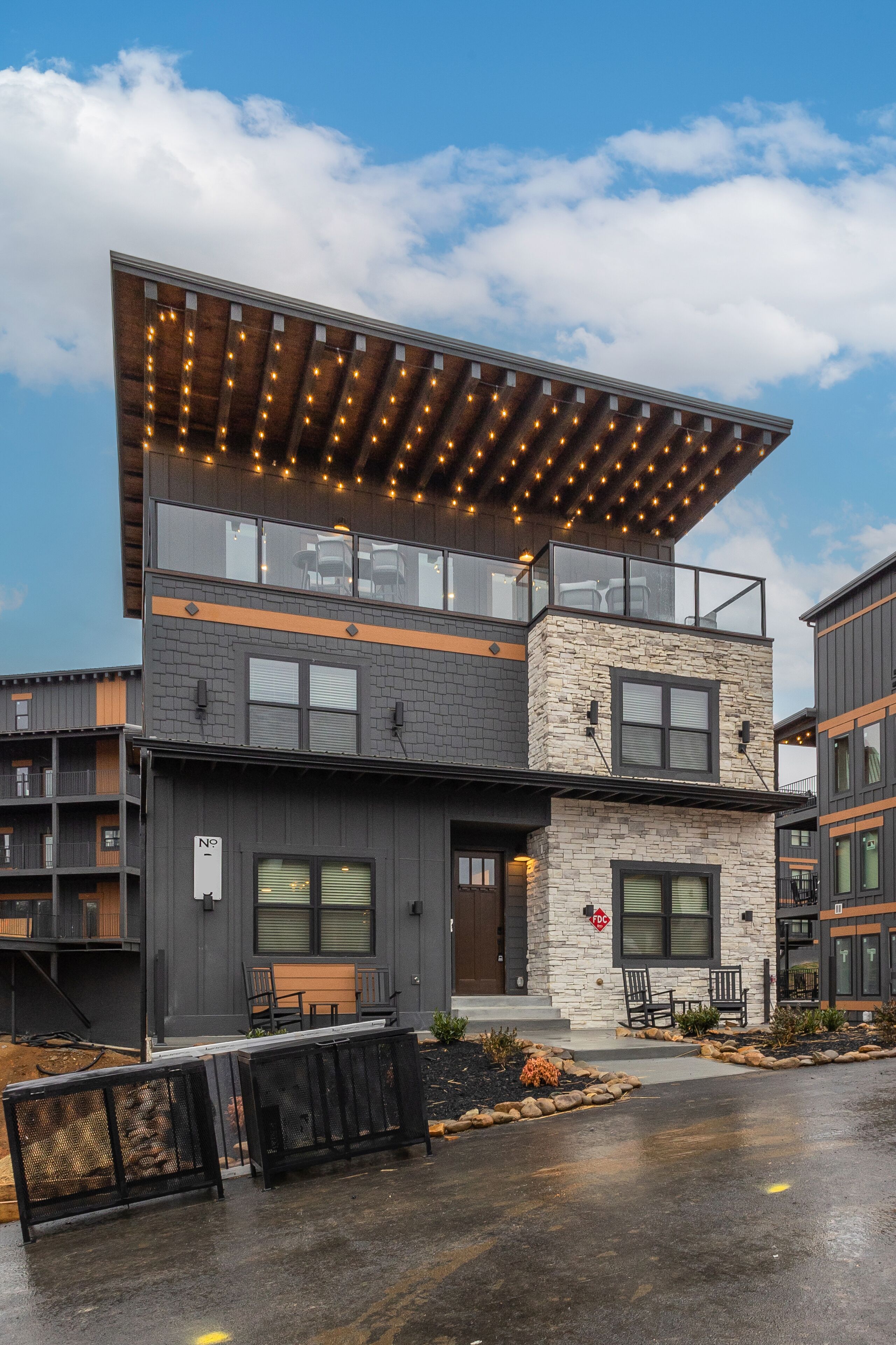 A modern two-story building with a stone facade, large windows, and a covered outdoor seating area.