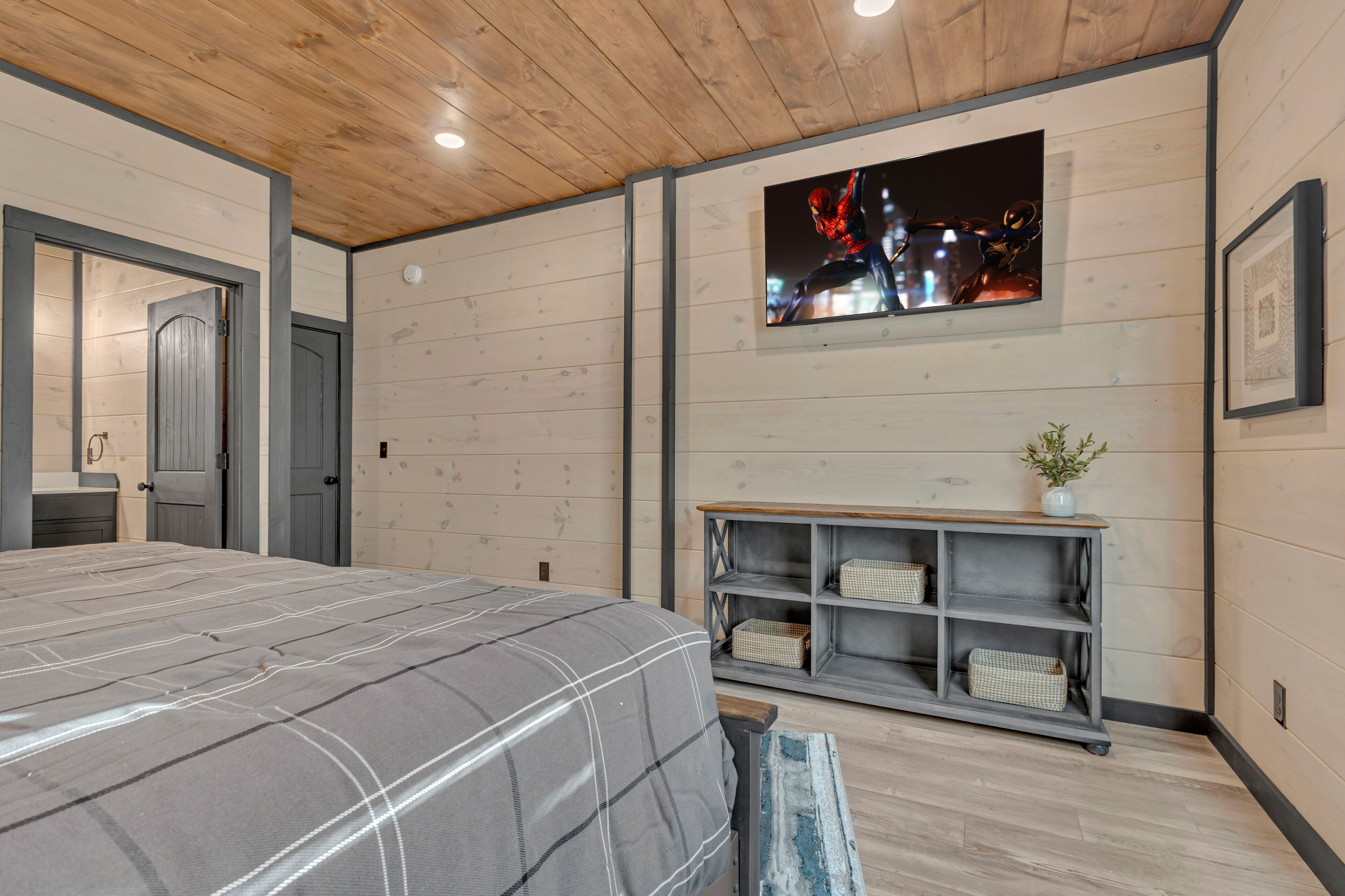 Een slaapkamer met een bed, een aan de muur bevestigde televisie, een houten plafond en een klein plankje met manden.