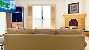 A living room with a sofa, television, ceiling fan, fireplace, and a view through a glass door. - Real Del Mar Tijuana  Apt for 2 guests (Tijuana)