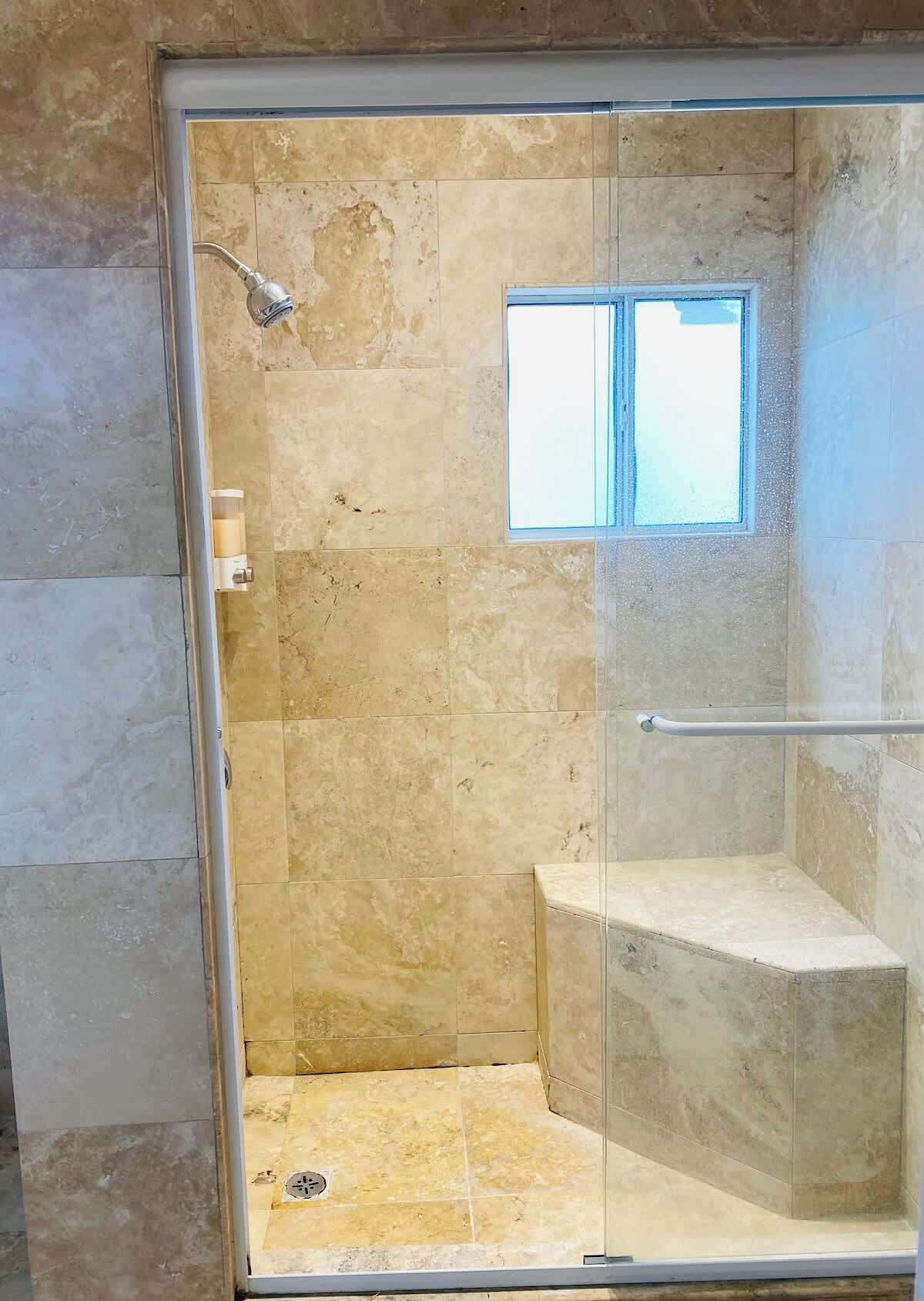 A glass-enclosed shower with a window, a handheld showerhead, and a glass door.