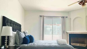 A bedroom with a bed, a nightstand, a lamp, a fireplace, and a view of the outside. - Real Del Mar Tijuana  Apt for 2 guests (Tijuana)