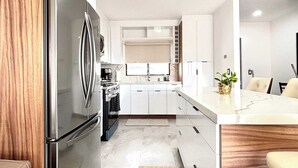 Una cocina moderna con armarios blancos, un refrigerador de acero inoxidable y una encimera de madera.