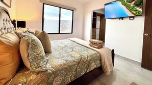 Un dormitorio con una cama grande, un televisor montado en la pared, una ventana con vista al mar y un armario.