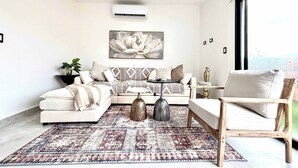 Una sala de estar moderna con un sofá, un sillón y una mesa de centro, un ventanal grande y una alfombra decorativa.