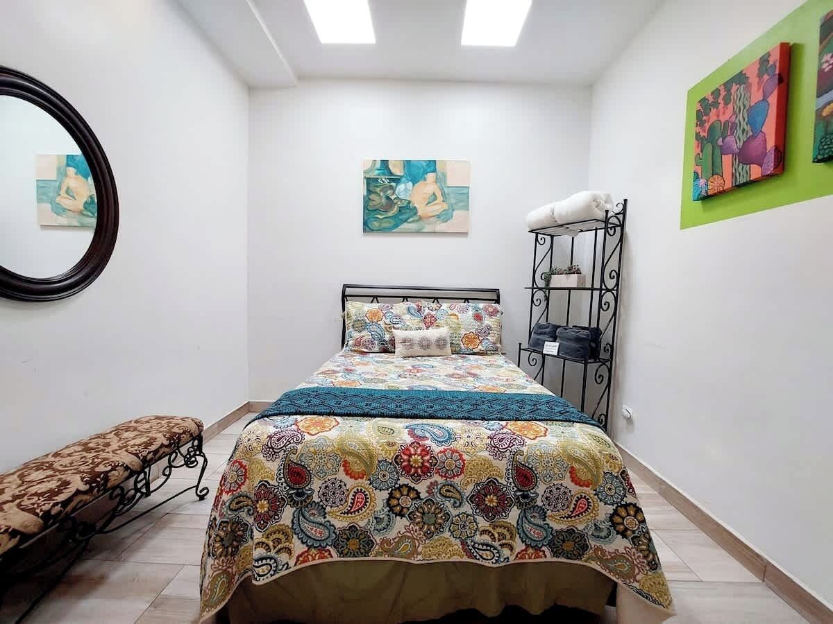 A bedroom with a bed, a bench, a circular mirror, and artwork on the walls.