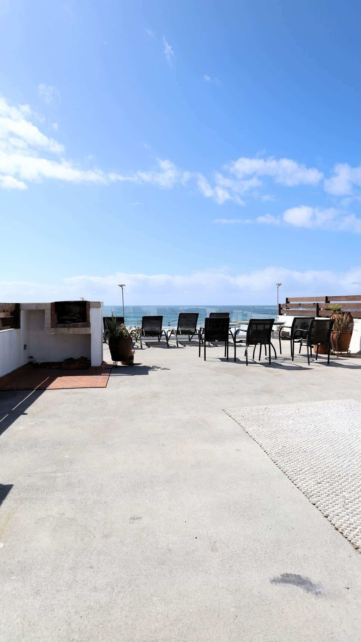 A rooftop patio with outdoor seating and a grill, overlooking the ocean.