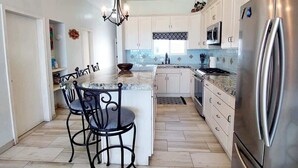 A modern kitchen with white cabinets, a stainless steel refrigerator, and a central island with two chairs.