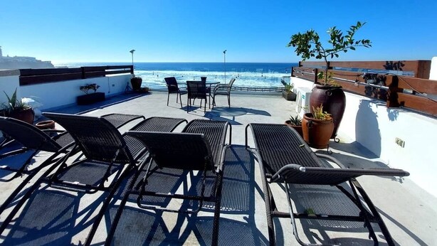 A rooftop terrace with black lounge chairs, potted plants, and a view of the ocean.