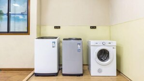 A laundry room with three appliances: a dryer, a stacked washer, and a front-loading washer. - Peace & Ease Hotel (Suzhou Jinji Lake Expo Center) (Suzhou)