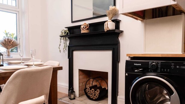 A dining area with a fireplace, a washing machine, and a dining table set for two.