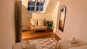 A cozy bedroom with a sloped ceiling, a sofa, a mirror, and a potted plant.