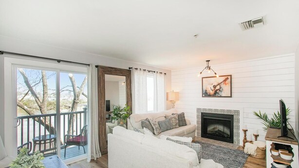 A living room with a fireplace, a sofa, a coffee table, and a balcony with chairs. - Downtown Riverside Condo with Pool. (Nashville)