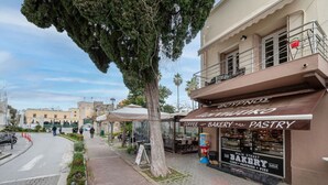 A street view with a bakery and coffee shop, outdoor seating, and a historic building in the background.