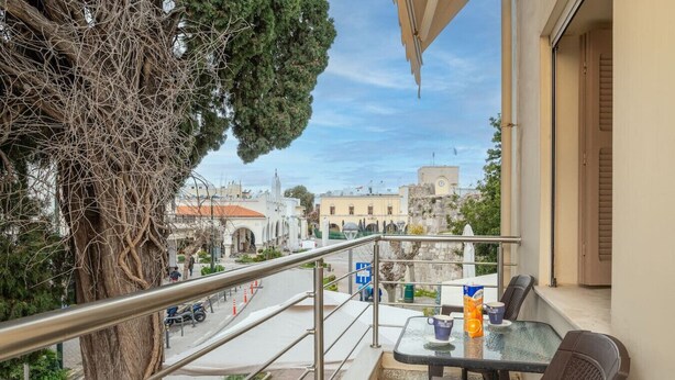 A balcony with a table and chairs, overlooking a street with buildings and a church.