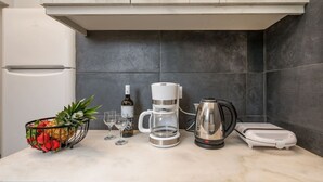 A kitchen with a white refrigerator, a coffee maker, a kettle, a fruit basket, and wine glasses.