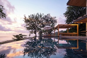 A modern infinity pool with a clear view of the ocean, a wooden deck, and a covered seating area with umbrellas. - Villa Nof Yam Luxury Villa Santa Teresa (Cobano)