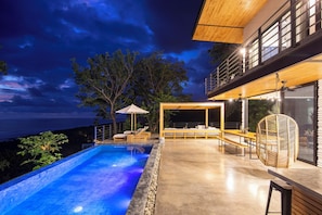 A modern outdoor pool area with a view of the ocean, wooden deck, and lounge seating. - Villa Nof Yam Luxury Villa Santa Teresa (Cobano)