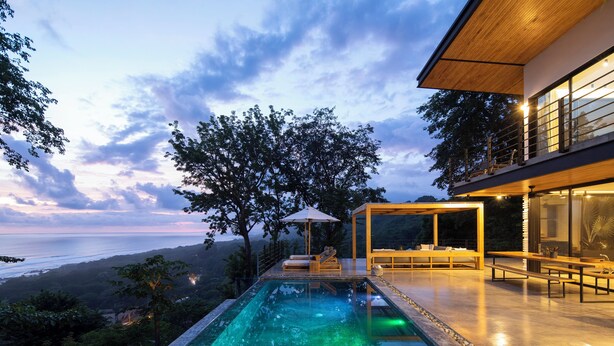 A modern outdoor pool area with a view of the ocean, surrounded by lush greenery and a wooden deck. - Villa Nof Yam Luxury Villa Santa Teresa (Cobano)
