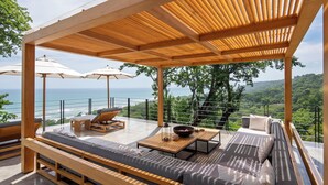 A modern outdoor seating area with wooden furniture, a large bowl, and umbrellas, overlooking a scenic ocean view. - Villa Nof Yam Luxury Villa Santa Teresa (Cobano)