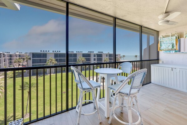 Ein Balkon mit Korbstühlen und einem kleinen Tisch, mit Blick auf eine Rasenfläche und ein mehrgeschossiges Gebäude.
