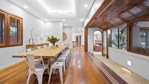 A modern dining area with a long wooden table, white chairs, and a central plant.