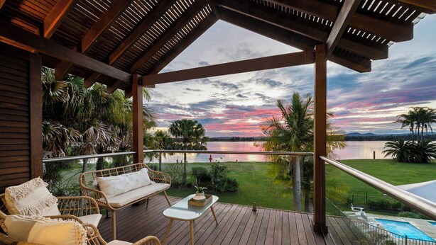 A wooden deck with wicker furniture and a view of a lake at sunset.