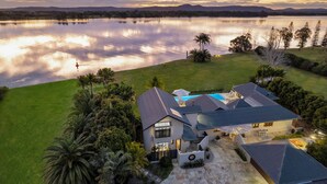 A modern house with a swimming pool, surrounded by lush greenery and a large body of water.