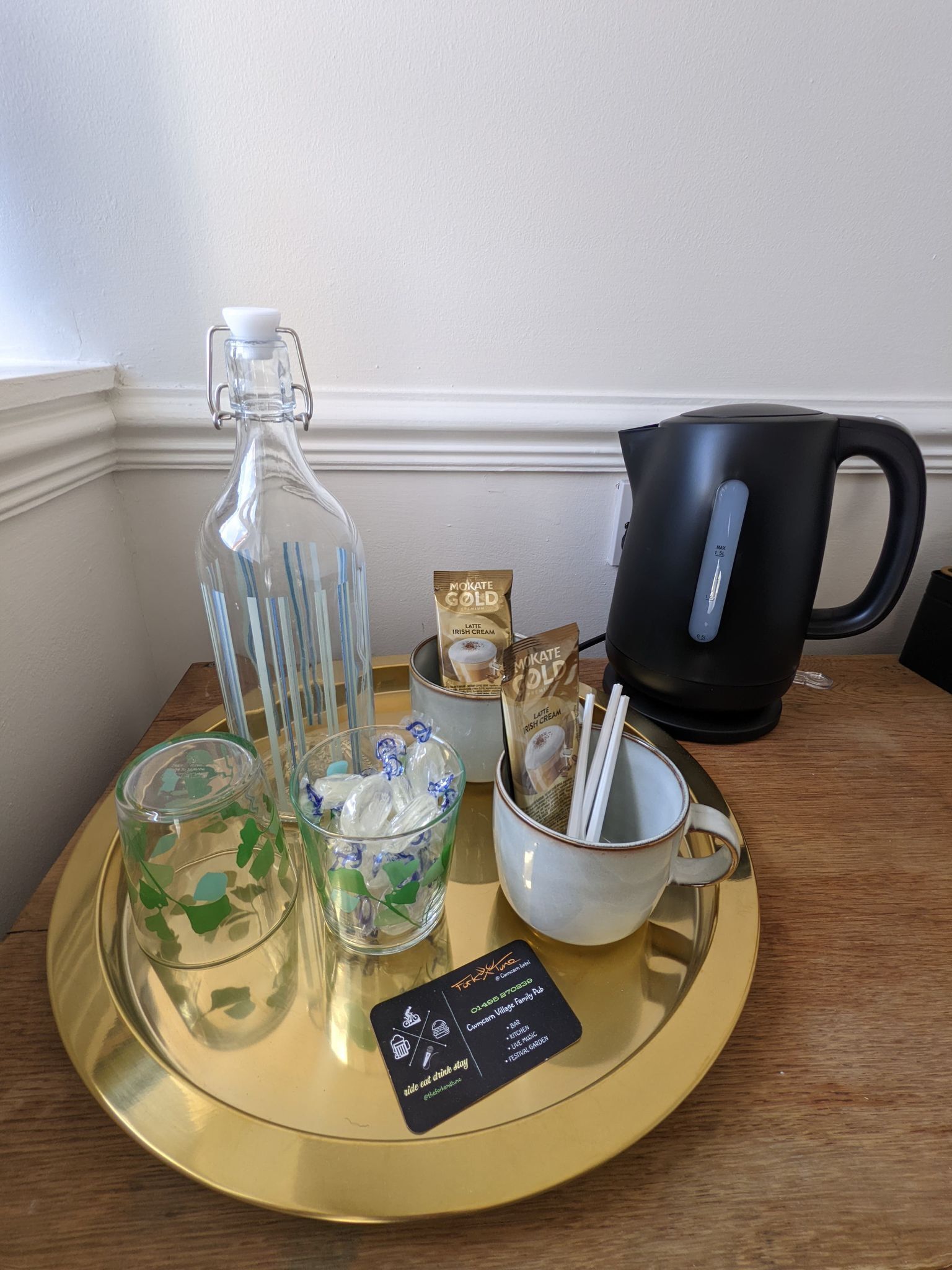 Een dienblad met een glazen fles, twee glaasjes, een mok en een pak koffie op een houten tafel.