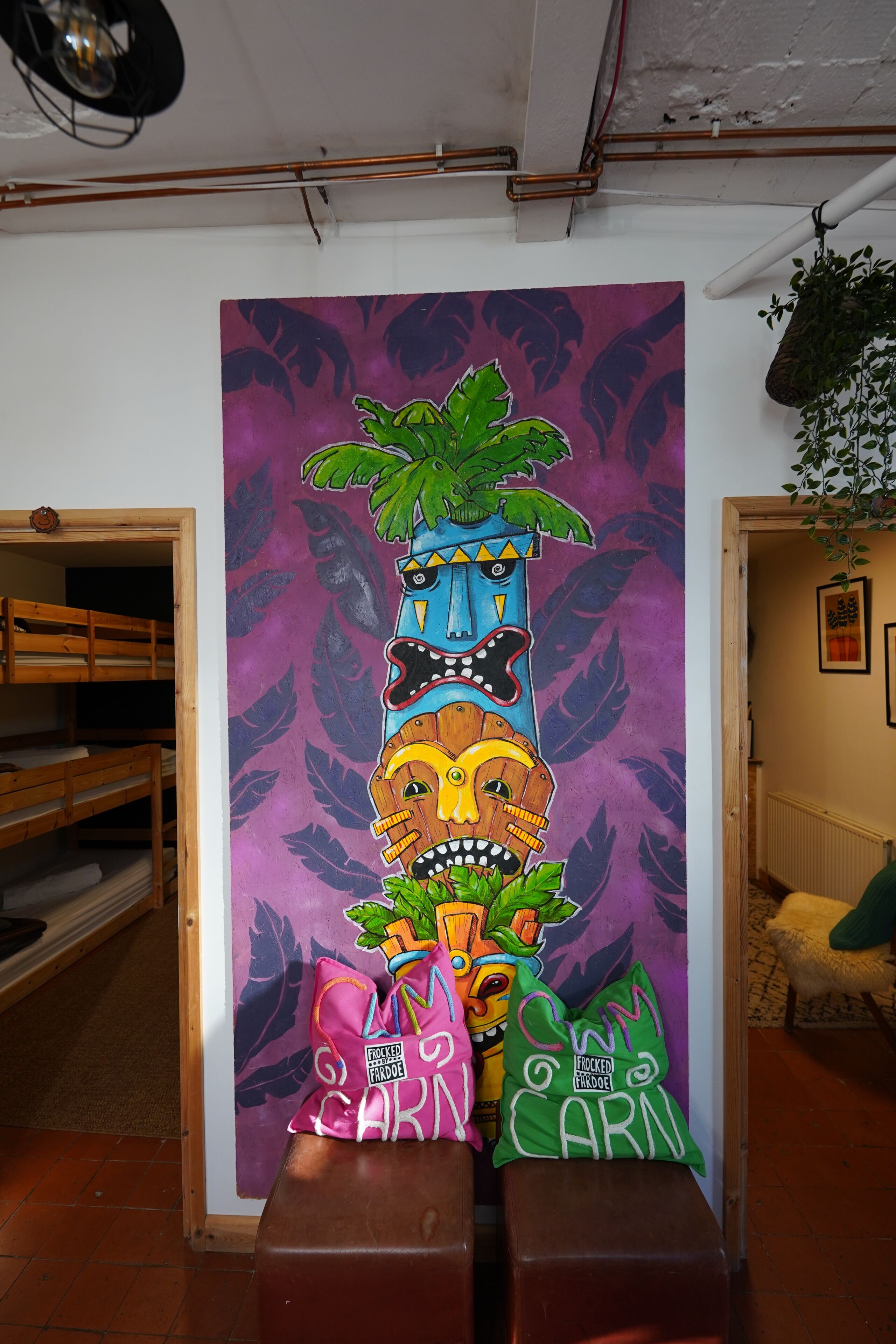 Une pièce décorée d’une fresque murale colorée, avec des lits superposés en bois et une plante suspendue.