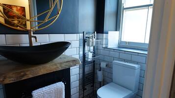 A bathroom with a black and white patterned floor, a white toilet, a black sink with a white towel, and a window with hanging plants.