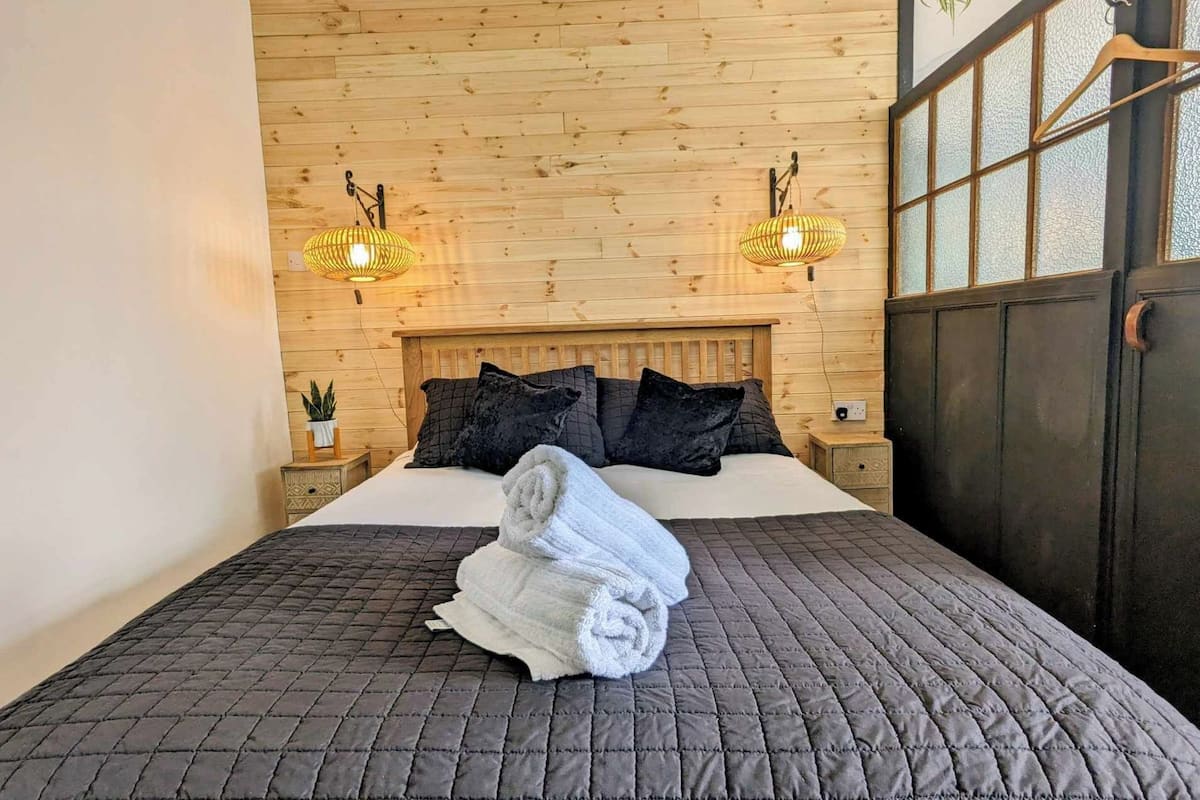 A wooden-paneled room with a bed, two wall-mounted lamps, and a window with a frosted glass view.