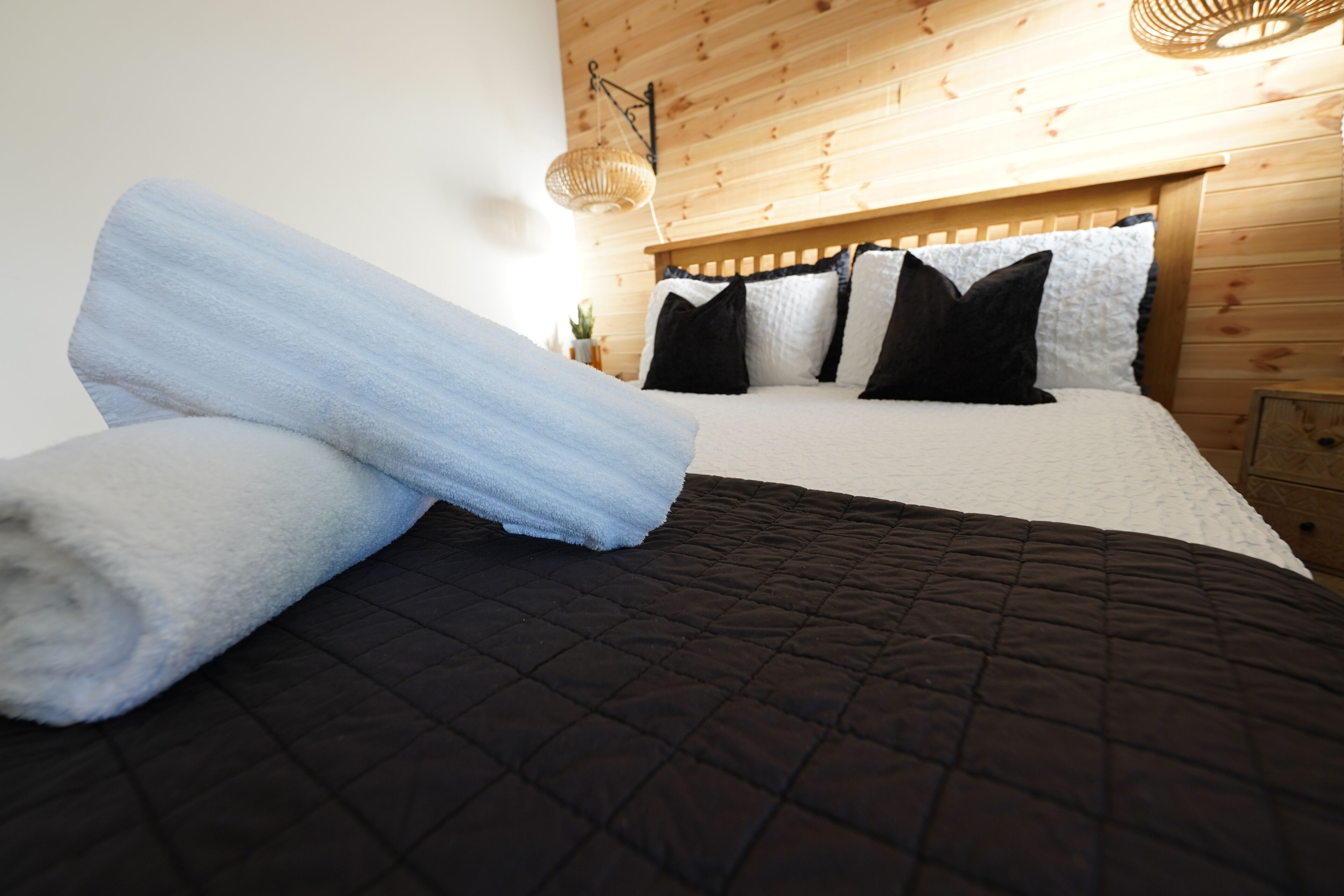 Una cama con colcha oscura, una toalla azul y almohadas negras.