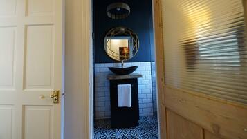 A bathroom with a white door, a black sink, a round mirror, and a patterned floor.